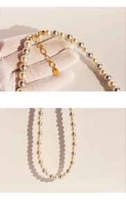 Detail of white and champagne grey pearl necklace with gold clasp and brand tag