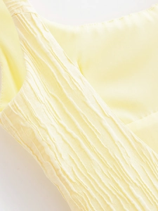 Macro shot of light yellow fabric showing detailed vertical pleated texture and soft material