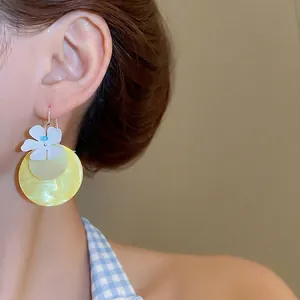 Fresh yellow shell disk earrings with white floral accent and blue bead on model