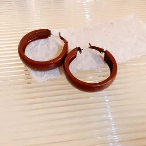 Close-up of elegant maroon glossy hoop earrings resting on textured rustic paper background