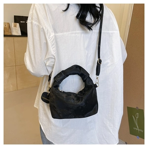 Detail of black pleated crossbody bag featuring knot handle and circular fashion tag