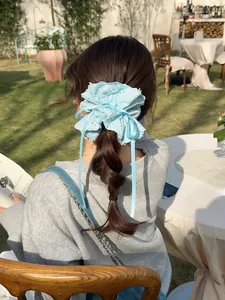 Detail of light blue embroidered lace scrunchie with ribbons shown in a garden setting