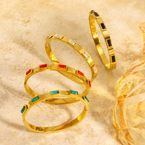 Quatre bracelets joncs dorés ornés de zircons rectangulaires colorés sur fond de marbre