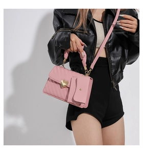 Pink pleated handbag with heart buckle and matching pouch shown on a model in black outfit