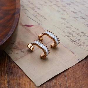 Close-up of gold C-shaped earrings with baguette-cut zircon on vintage paper background