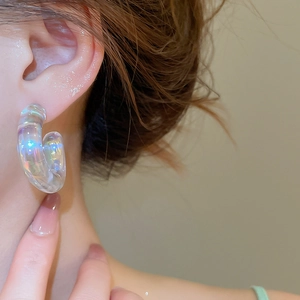 Macro shot of iridescent round C-shape acrylic earrings worn on a model's ear