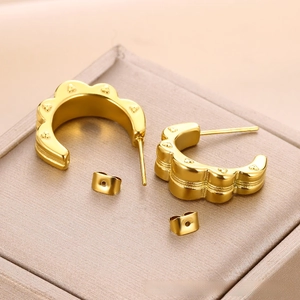 Detail view of gold wave-shaped C earrings with tiny heart patterns on a textured surface