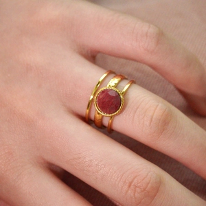 Macro detail of stacked 14k gold plated rings featuring a natural red gemstone centerpiece