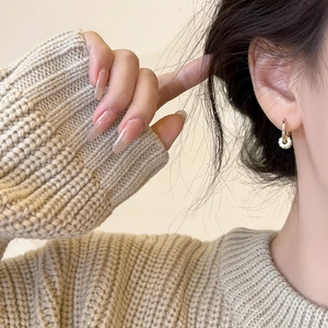 Close-up of 18k gold plated hoop earrings with textured pendants on a model's ear
