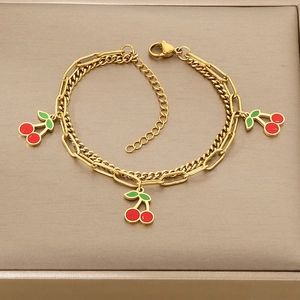 Detailed macro of gold double-layer chain bracelet featuring three enamel cherry charms