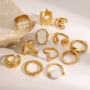 Flat lay of multiple gold rings featuring pearls and shells on natural stone props