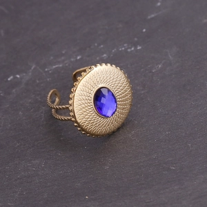 Détail d'une bague dorée vintage avec pierre bleue et texture radiale sur socle en pierre