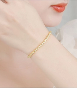 Close-up of a 2mm gold moissanite tennis bracelet worn on a woman's wrist