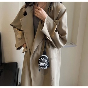 Close-up of zebra pattern mini bag with logo patch worn over a classic khaki trench coat