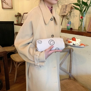 Close-up of white corduroy smile cosmetic bag held by hand in a cozy cafe setting