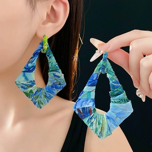 Detailansicht der blau-grünen Stoffohrringe in Rautenform an einem Modell vor schwarzem Hintergrund