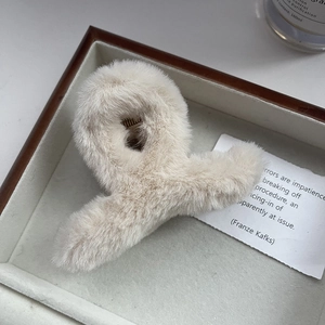 Dettaglio di una pinza per capelli in peluche beige su un vassoio di legno con luce morbida