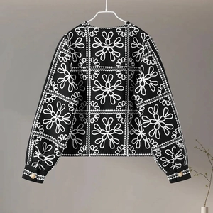 Detail of black long-sleeve top with white geometric floral embroidery and gold button cuffs