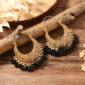 Détail de boucles d'oreilles créoles dorées avec pampilles en perles noires sur bois rustique