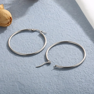 Polished silver large hoop earrings in stainless steel on a minimalist blue background