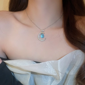 Close-up of a silver crescent moon necklace with a blue teardrop zircon on a model