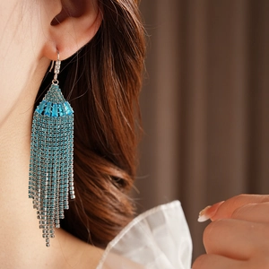 Detail of blue rhinestone fan-shaped tassel earrings worn by a model in soft lighting