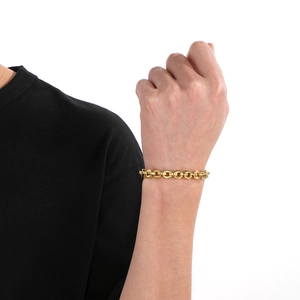 Detailed view of a gold chain link bracelet worn by a model on a white background