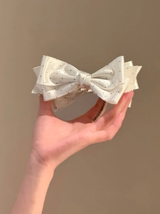 Close-up of cream polka dot bow hair clip with sparkling rhinestone centerpiece decoration