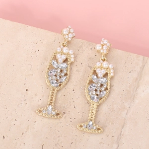 Detail of champagne glass earrings with pearls and rhinestones on marble background