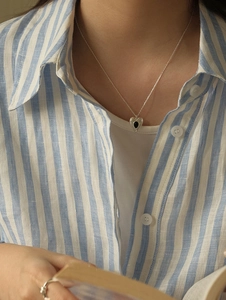 Close-up of heart-shaped silver necklace with black enamel pendant on a model wearing stripes