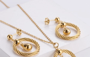 Macro shot of polished gold-plated teardrop jewelry set on white stone texture background