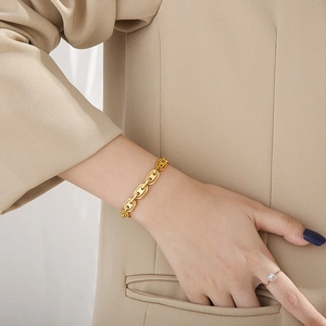 Close-up of gold coffee bean chain bracelet and gem ring on model wearing beige suit