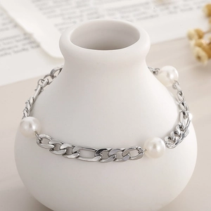 Detail of silver chain bracelet with white pearls draped on a white ceramic vase
