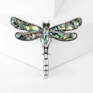 Vintage dragonfly brooch with iridescent abalone shell wings on a white pedestal