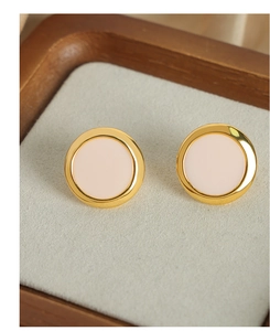 Macro detail of elegant round gold-plated stud earrings with soft pink inlay on a tray