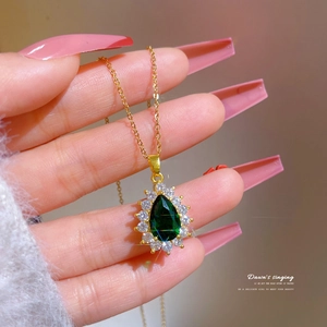 Detailed view of teardrop green emerald pendant with crystal halo on titanium steel necklace