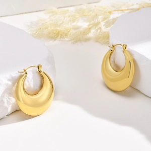 Detailed view of gold hollow teardrop earrings on a white textured stone background