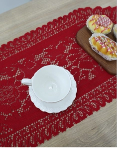 Detailed texture of a red crochet lace Christmas table runner on a wooden surface