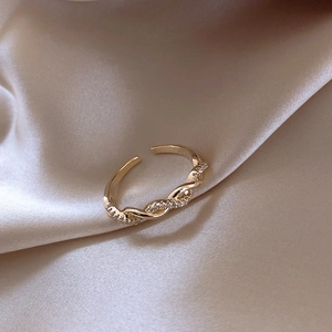 Close-up of golden twisted braided ring featuring sparkling zircon inlay on silk background