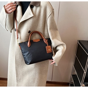 Detail of nylon tote bag with leather handles and crossbody strap on beige coat