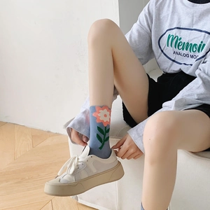 Detail shot of blue crew socks featuring pink floral patterns and green leaves on the model