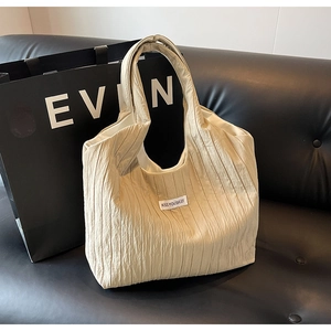 Detail der cremefarbenen Plissee-Tasche mit aufgenähtem Etikett auf schwarzem Sofa
