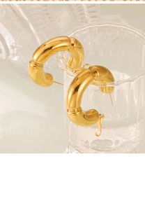 Detailed view of hollow gold bamboo-style C-shaped earrings hanging on a glass rim