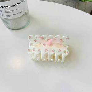 Detailed view of white acrylic hair claw with pink floral pattern and sheer ribbon bow