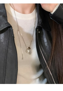 Close-up of tiger eye pearl pendant necklace worn with white knitwear and black jacket