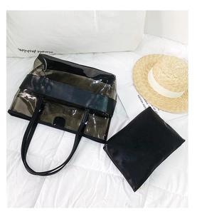 Detail of clear PVC tote and black insert bag set on white bedding with lifestyle props