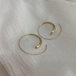Detail of matte gold spiral hoop earrings on elegant textured white fabric background