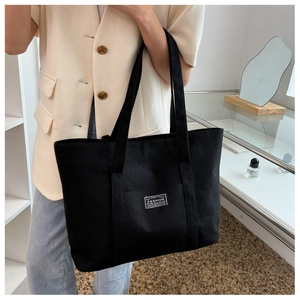 Close-up of black canvas tote bag on female model featuring stylish FASHION patch