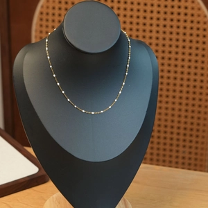Détail d'un élégant collier à chaîne fine dorée avec perles blanches sur un présentoir de cou