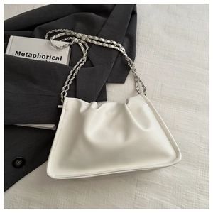Detail of white pleated cloud bag with silver braided chain strap on grey blazer